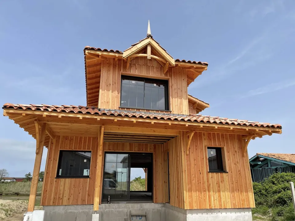 Façade de maison en bardage vertical avec avancée de toit et charpente apparente.