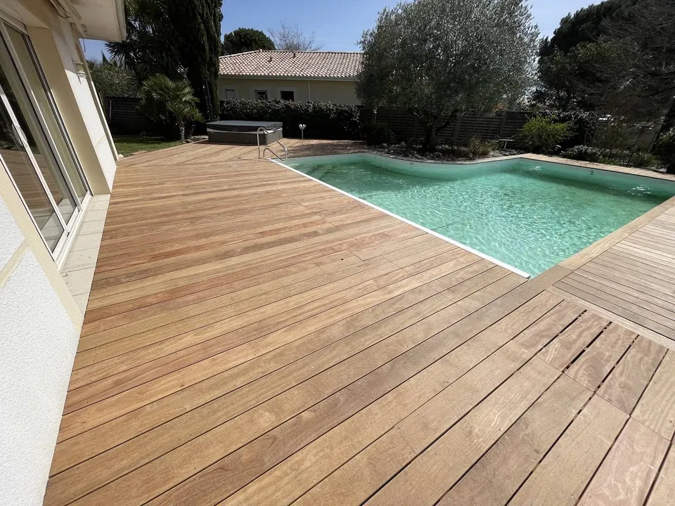 Grande terrasse en bois clair entourant une piscine extérieure.